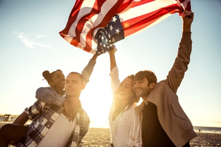 Four young people holding an American flag at the beach